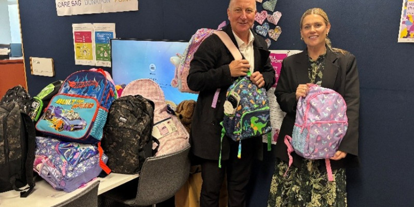Two adults in an indoor setting surrounded by colourful bags filled with basic necessities 