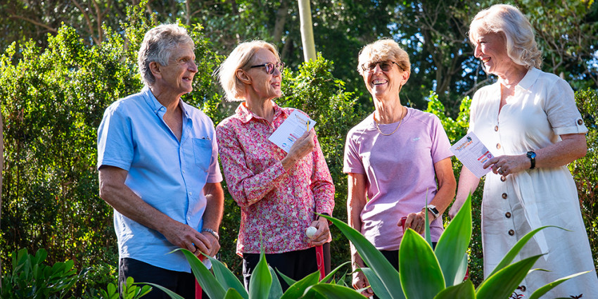 A group of four older people, smiling, well dressed, in a garden surrounding