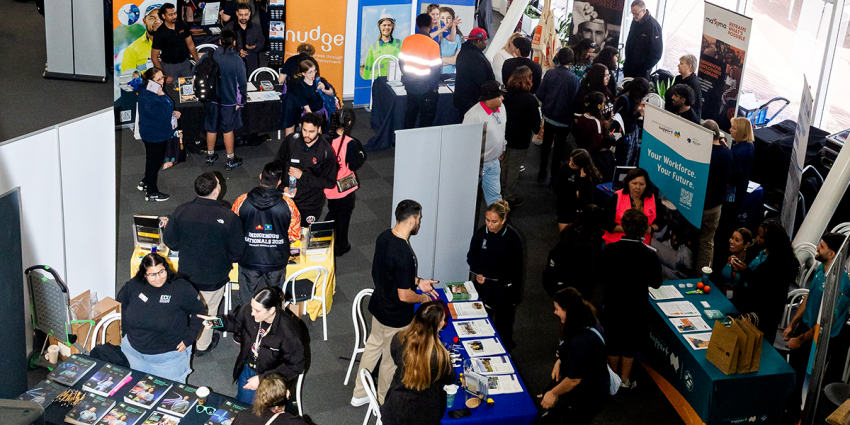 Busy Deadly Jobs Expo with attendees visiting exhibition booths, speaking with representatives, and browsing training and employment information.