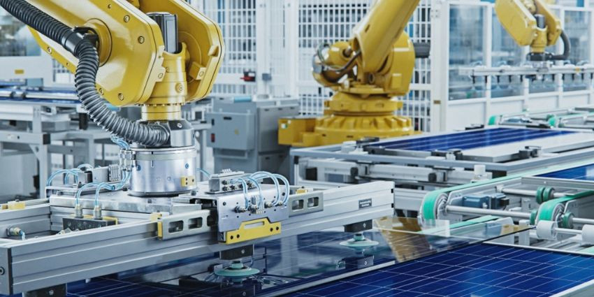 Two robotic arms manufacturing solar panels on a conveyor belt.