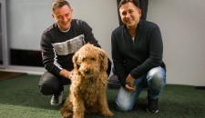 Image of two adult men and a dog, smiling and looking happy