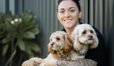 Image of a young adult woman smiling and hugging two pet dogs