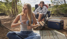 A woman sitting on the ground brushing her hair with a man sitting behind her watching