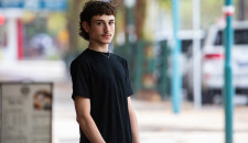 A young man wearing a tshirt, standing on the street