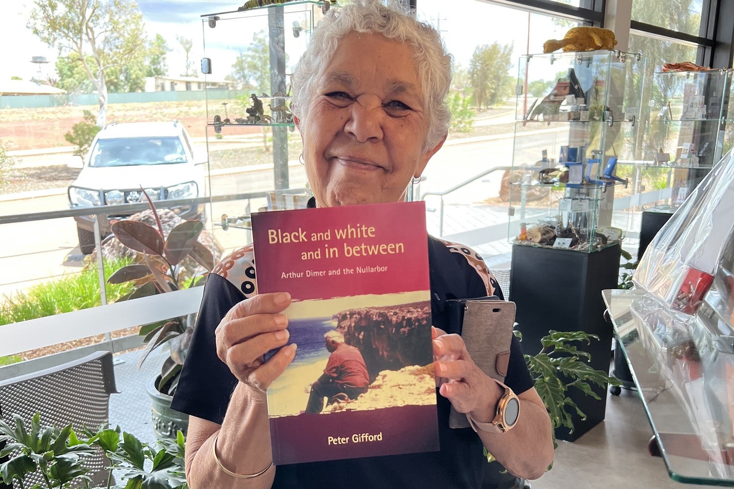 Photo of Communities staff member Wendy Dimer holding up a book called 'Black and white and in between' 