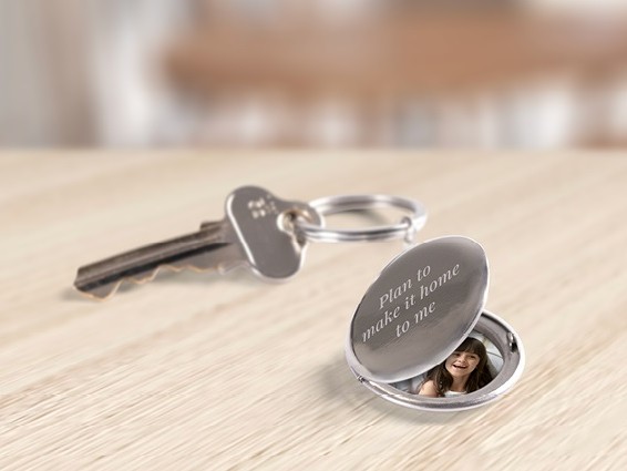 Image of a silver locket engraved with the words 'plan to make it home to me' sitting on a wooden table next to a metal key.